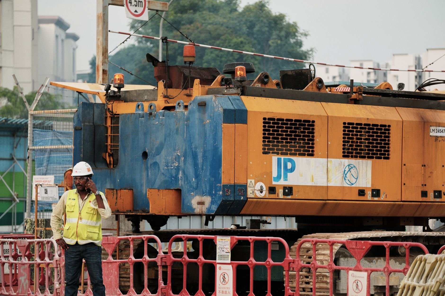 Worker on phone at construction site with large machinery in urban setting.
